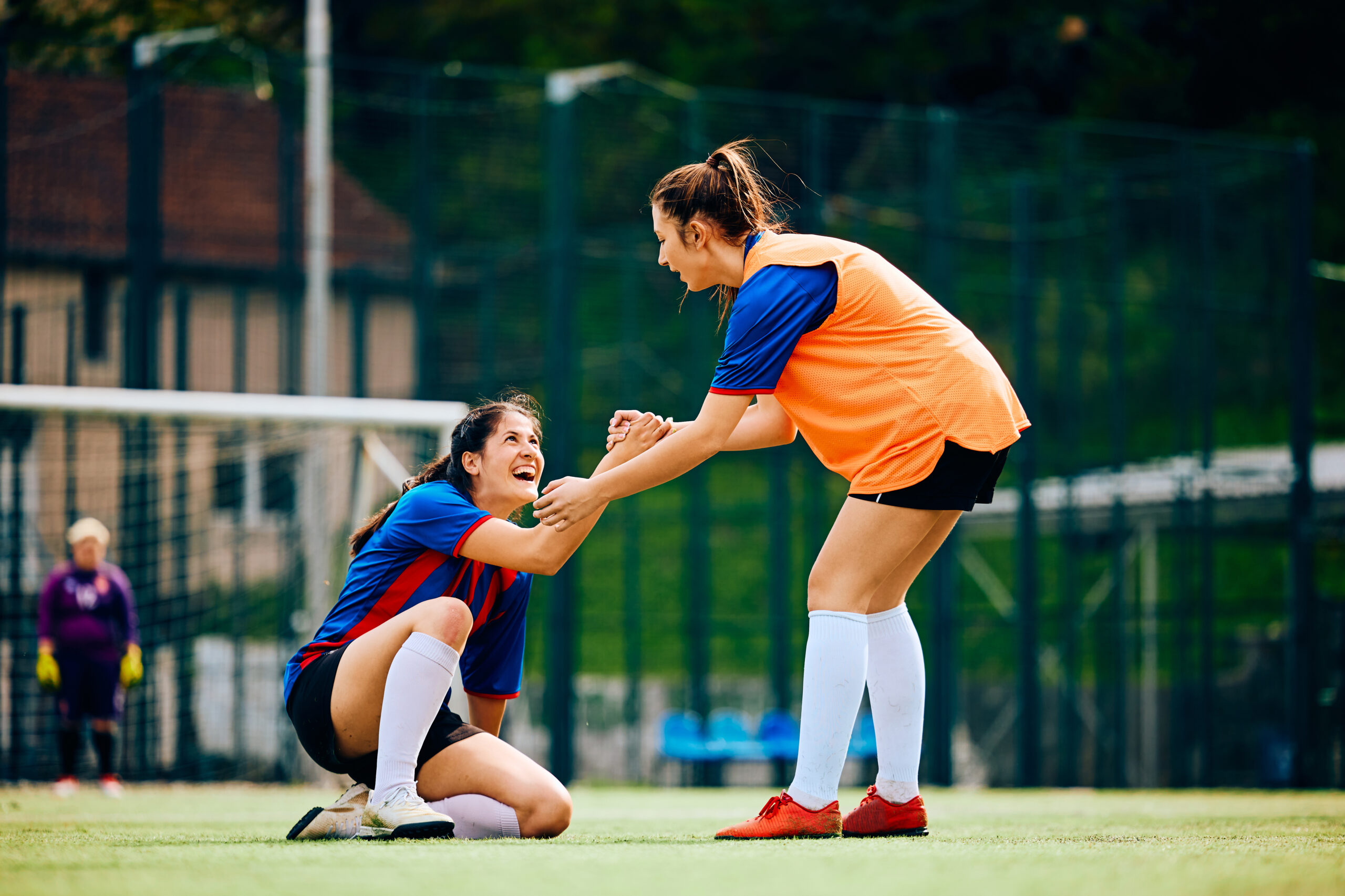 Happy soccer player assisting her teammate in getting up after a foul on playing field. Copy space.